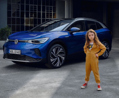 Femme en combinaison jaune posant à côté d'une voiture bleue moderne