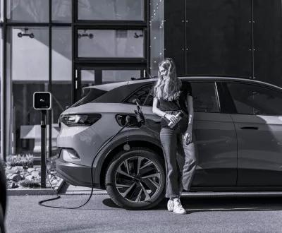 Photo en noir et blanc d'une femme qui recharge une voiture électrique