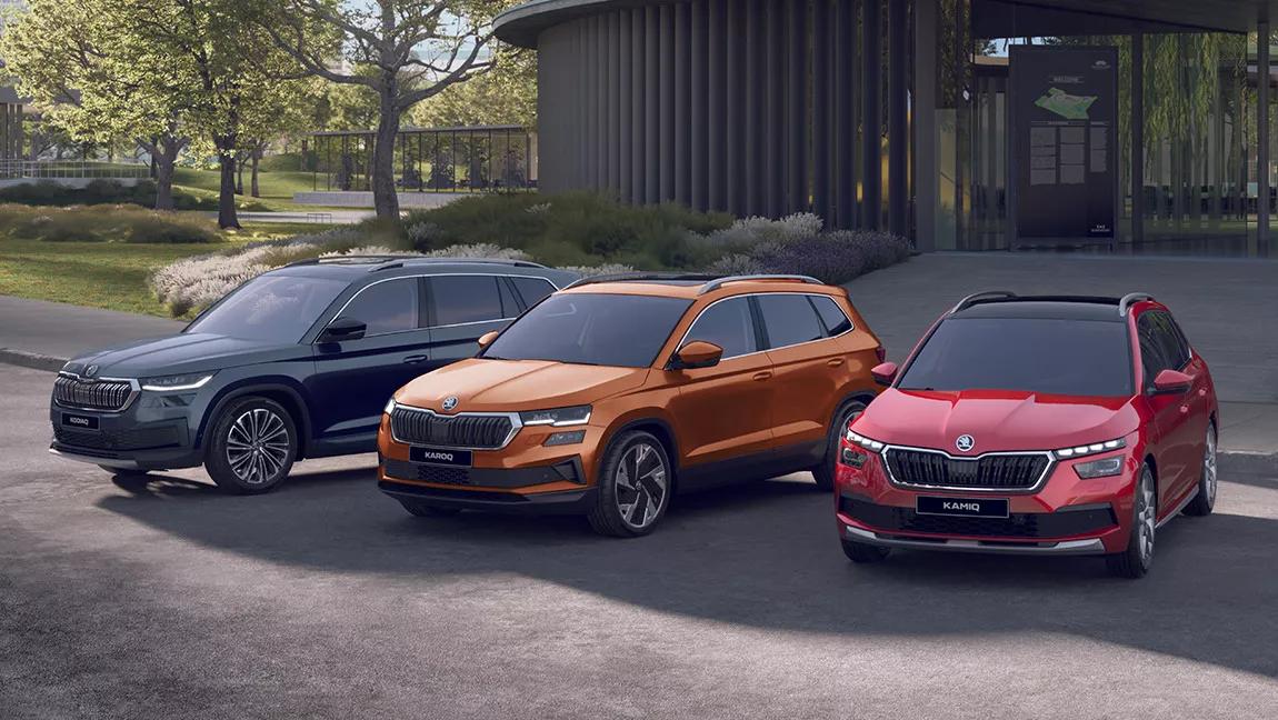 Trois voitures SUV Skoda noire, orange et rouge devant un bâtiment en verre