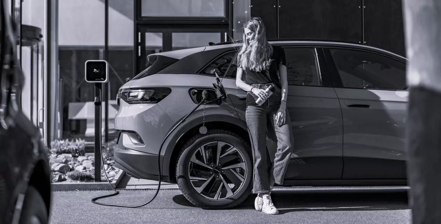 Photo en noir et blanc d'une femme qui recharge une voiture électrique