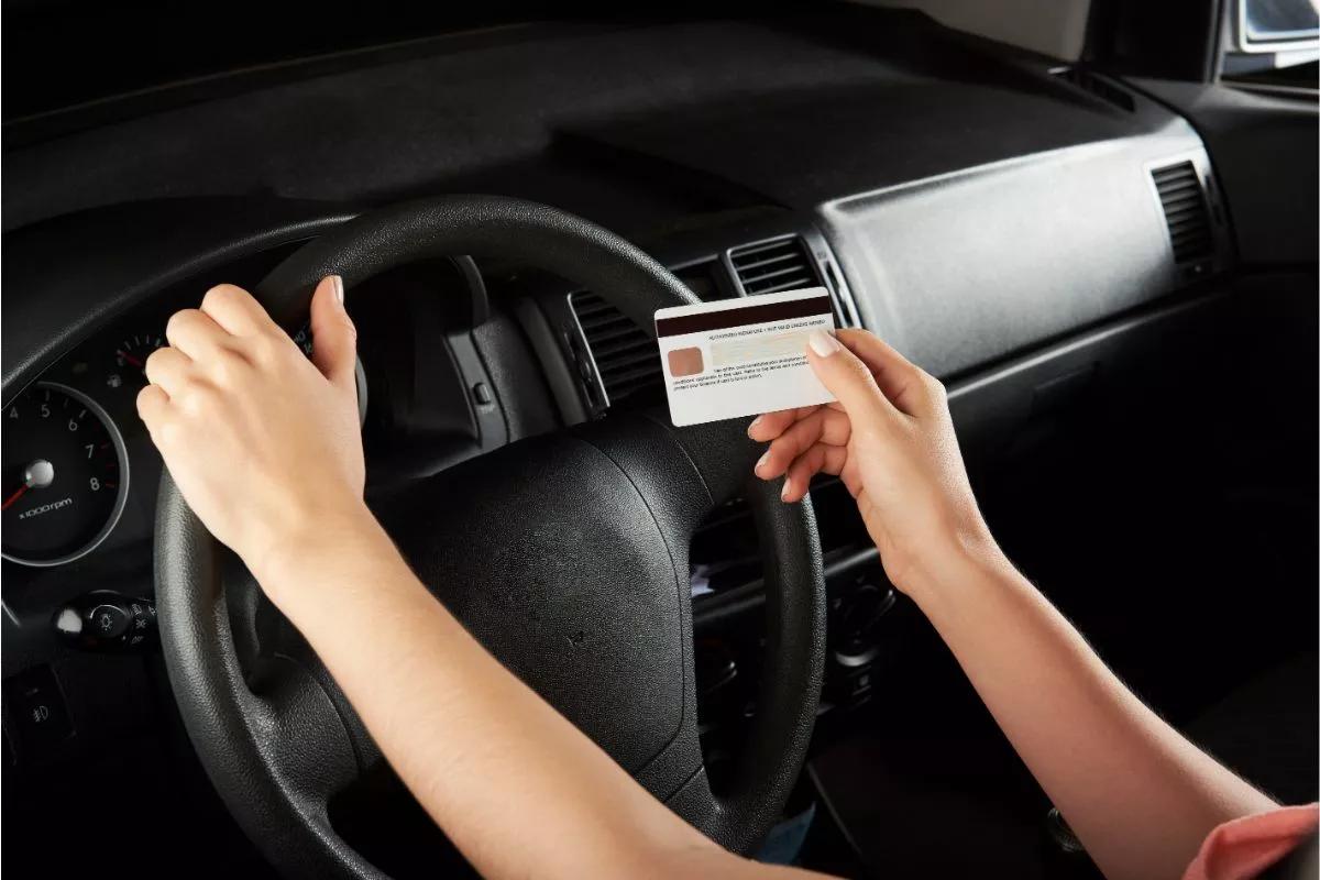 Mains tenant une carte de crédit sur le volant d'une voiture